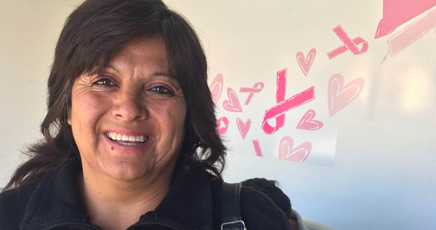 Smiling woman with dark hair in black jacket, pink ribbons and hearts in background